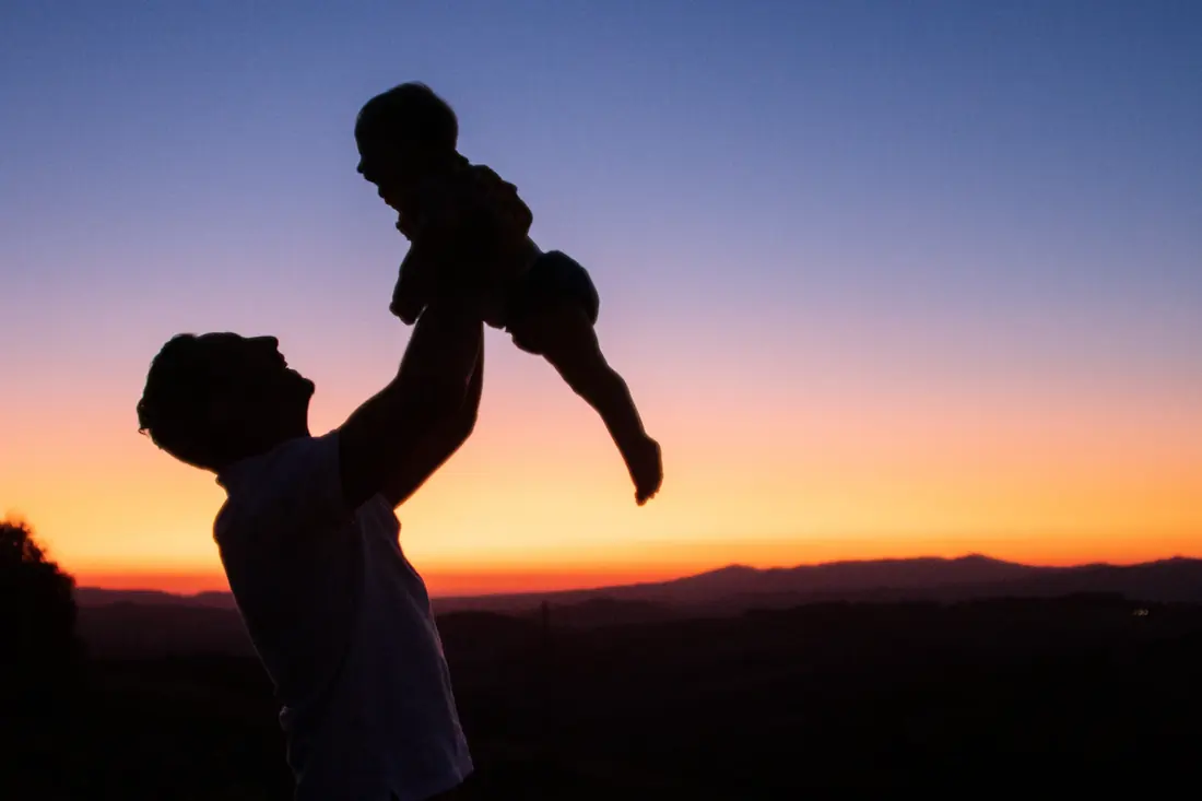 Silueta de un padre que levanta a su bebé frente a un cielo anaranjado